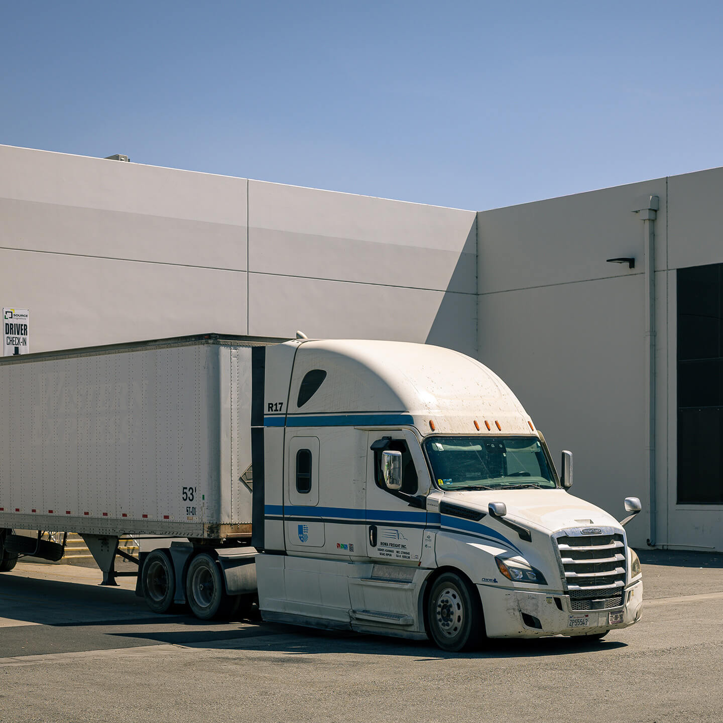 A semi-truck and trailer parked at the loading dock of a logistics warehouse.