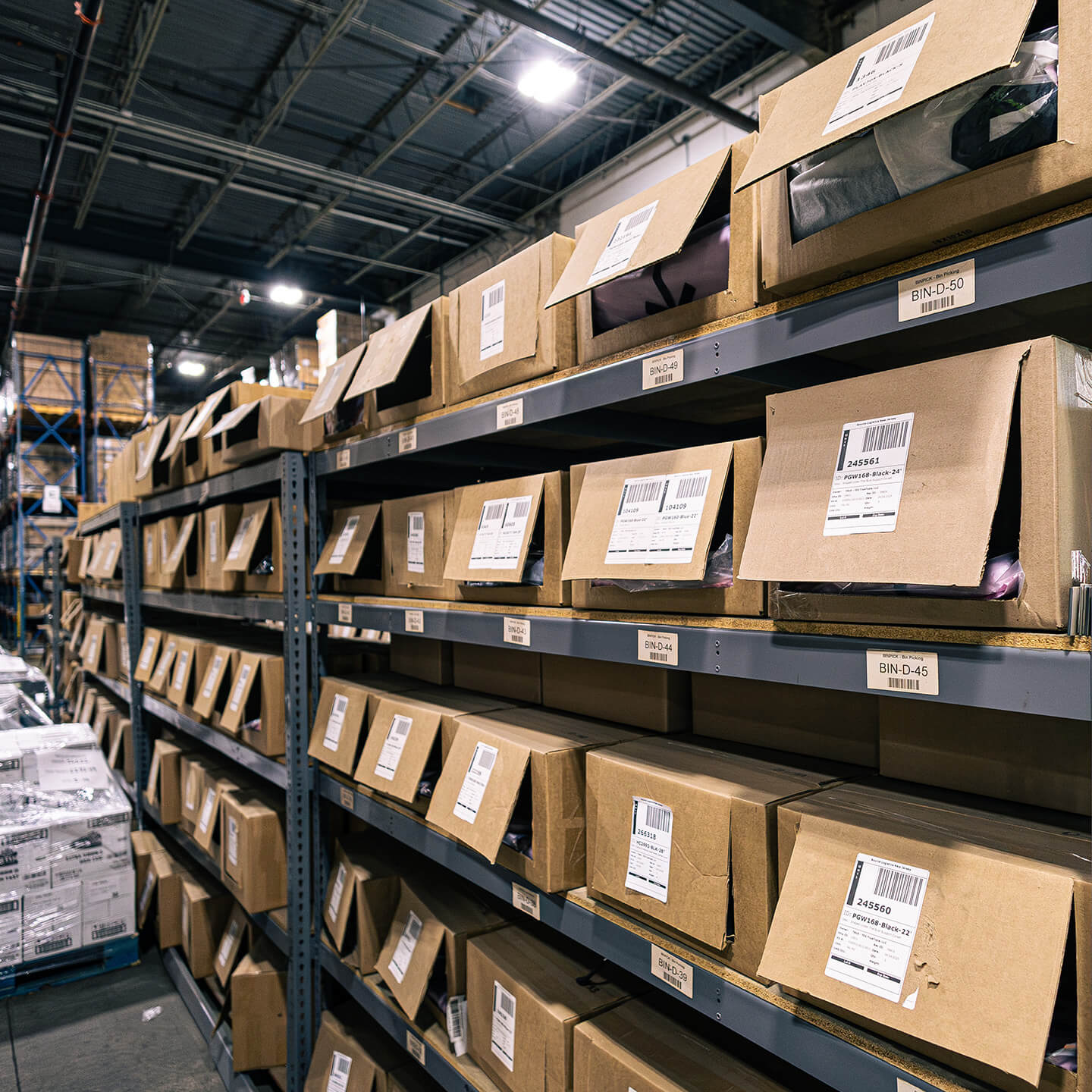 Close-up of organized warehouse shelving with brown boxes labeled with bin and inventory numbers.
