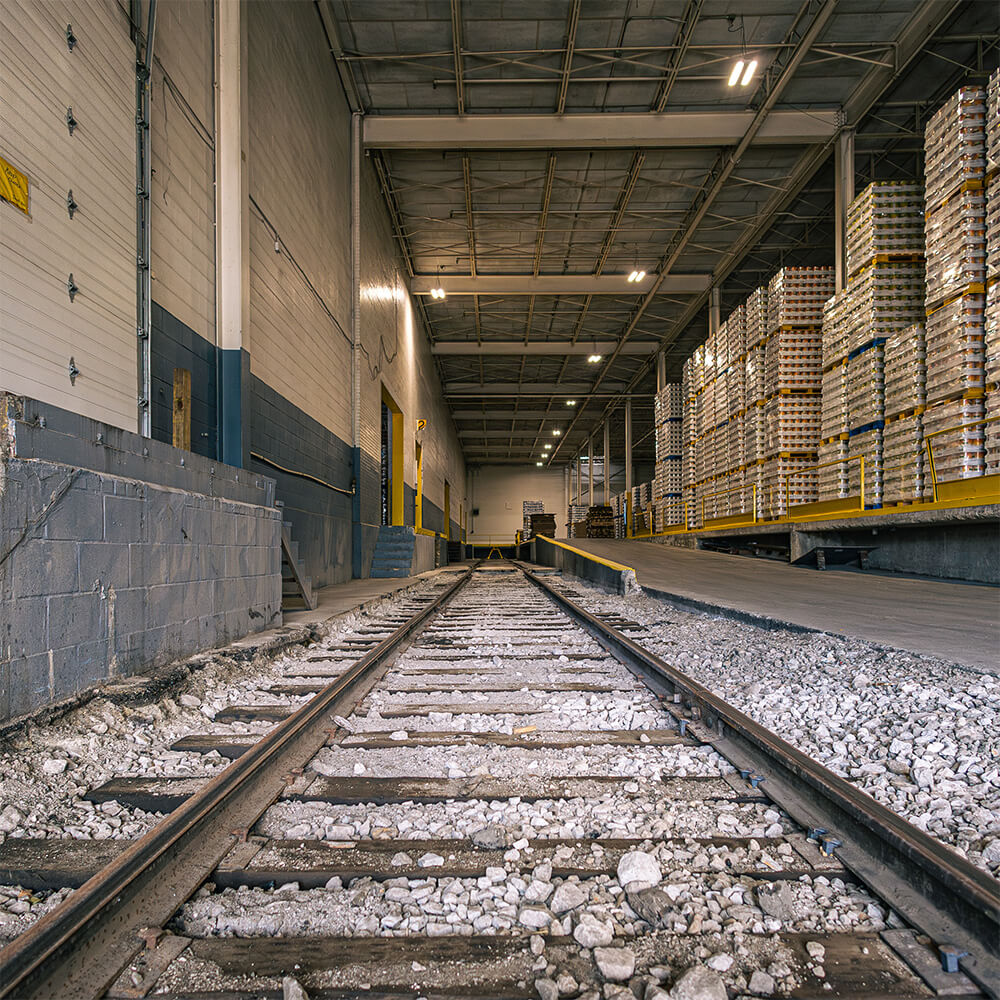 Low-angle view of railroad tracks leading into a large industrial warehouse.