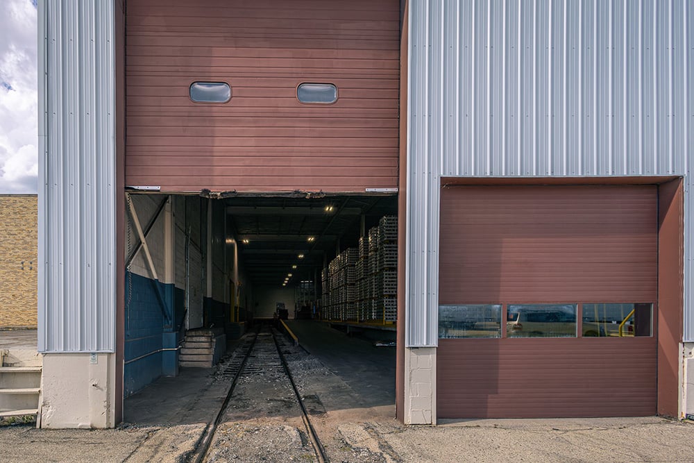 Exterior view of a warehouse featuring a large open bay door with railroad tracks leading inside.