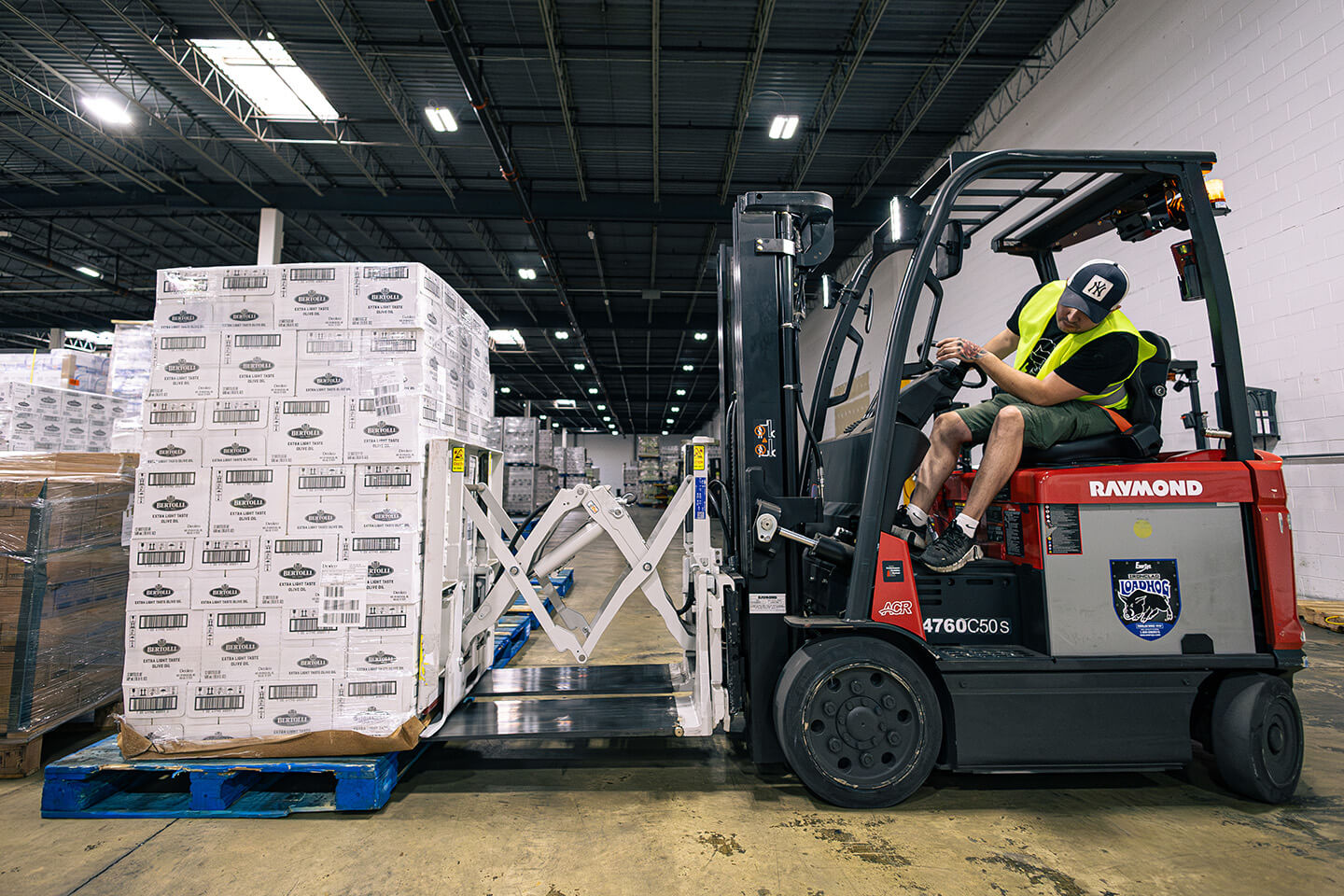 Forklift operator using a specialized push/pull attachment to handle a large pallet load in a warehouse.