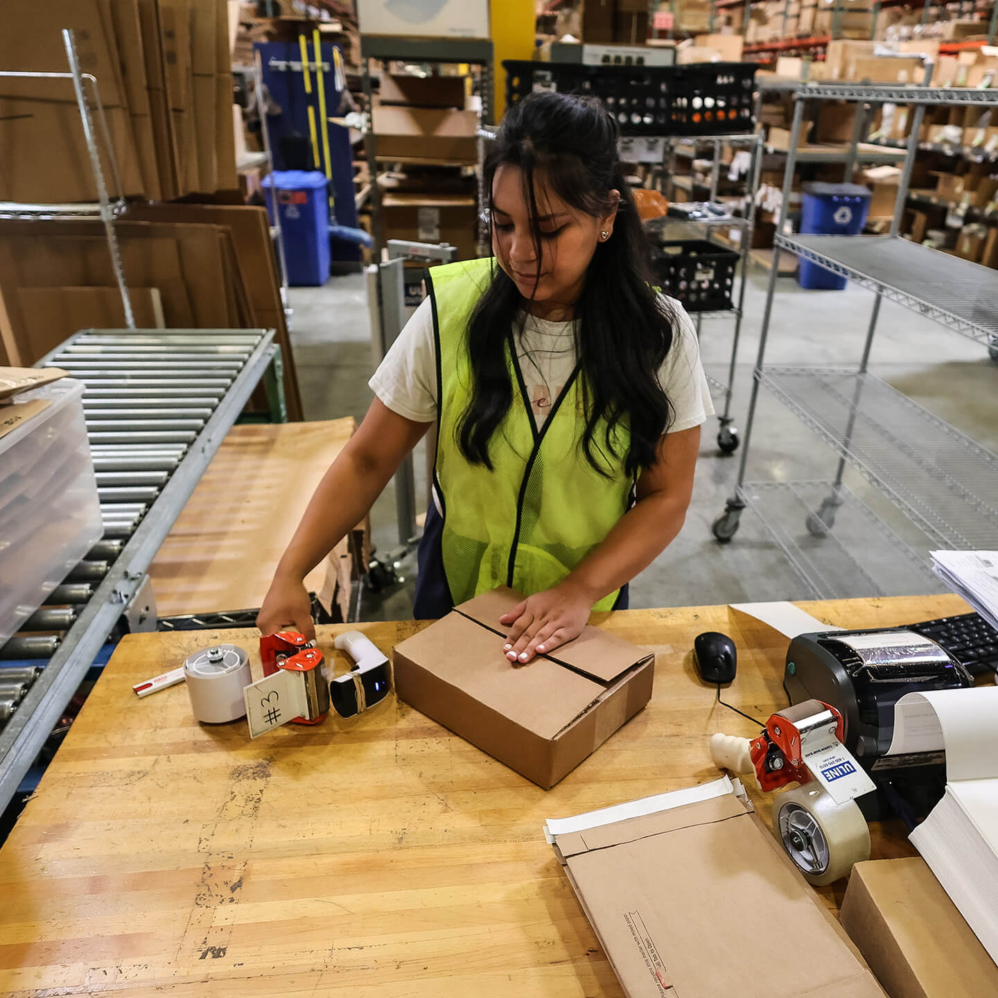 Warehouse worker packaging a small box for shipment at a fulfillment station.
