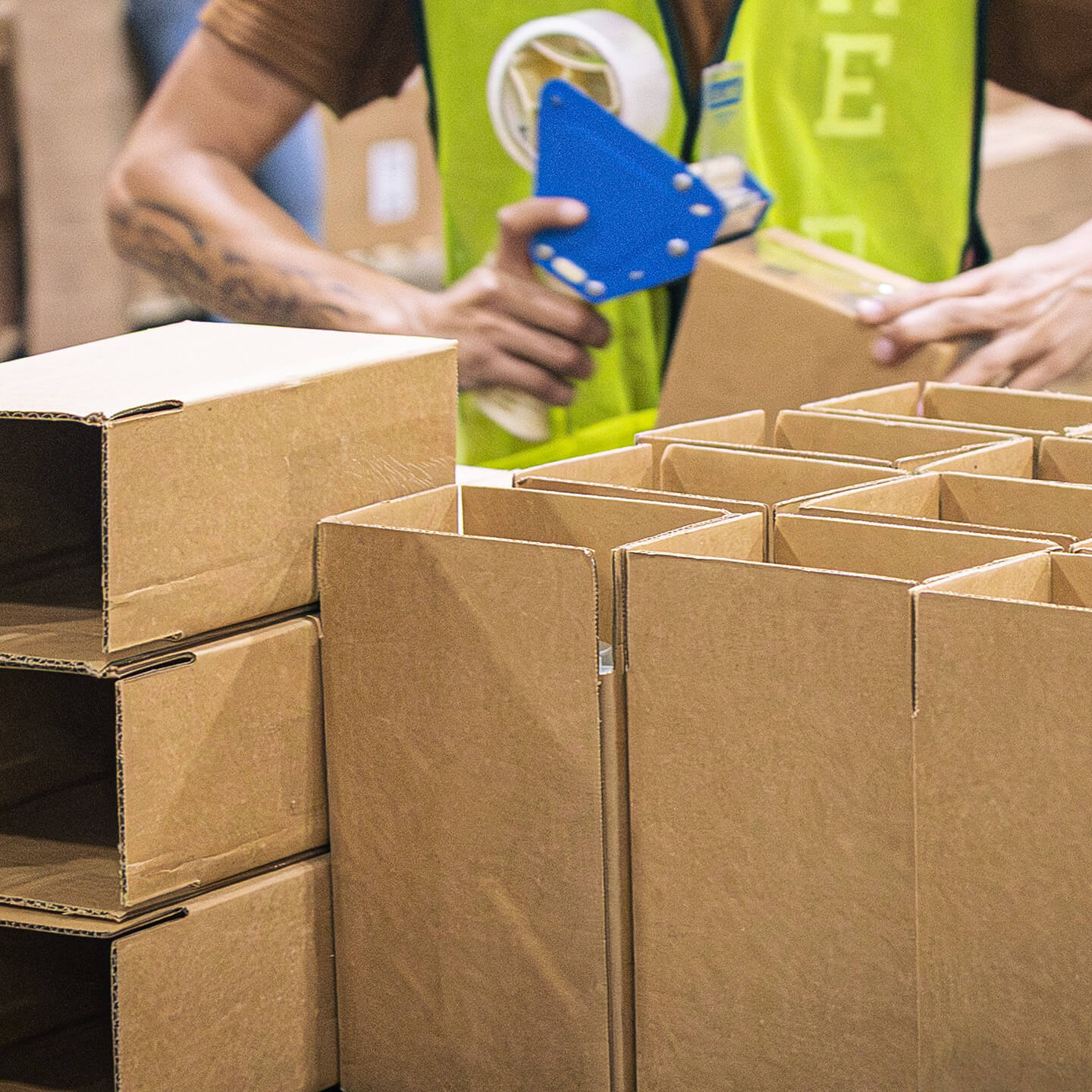 Logistics worker using a tape gun to assemble cardboard boxes for shipment.